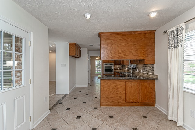 kitchen with tasteful backsplash, sink, kitchen peninsula, light tile patterned floors, and a textured ceiling