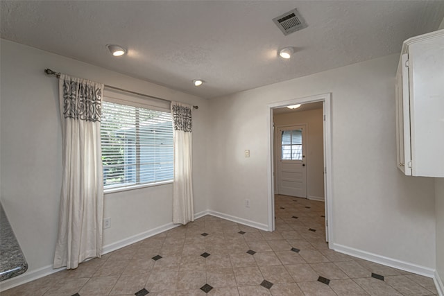 tiled empty room with a textured ceiling and plenty of natural light