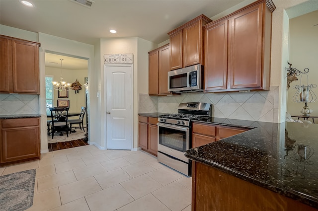 kitchen featuring appliances with stainless steel finishes, dark stone countertops, decorative backsplash, and a chandelier