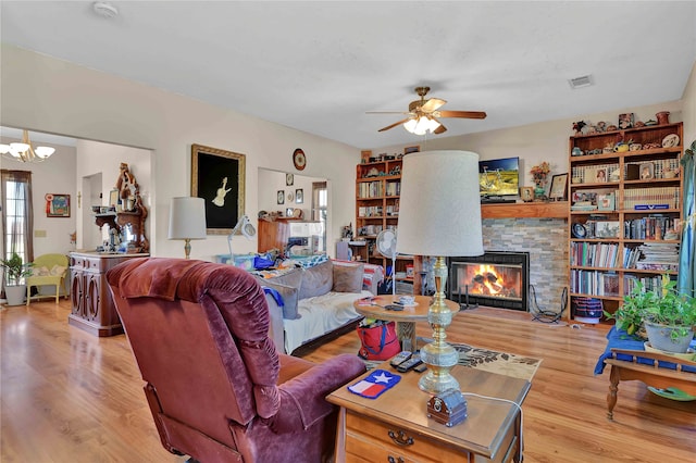 living room with a fireplace, light hardwood / wood-style floors, and ceiling fan with notable chandelier