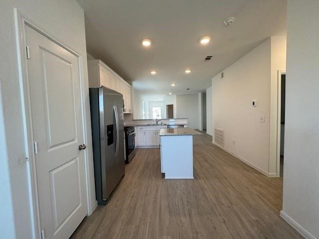 kitchen with hardwood / wood-style flooring, range, stainless steel refrigerator with ice dispenser, and white cabinetry