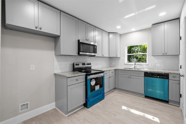 kitchen with light hardwood / wood-style floors, gray cabinets, tasteful backsplash, and stainless steel appliances