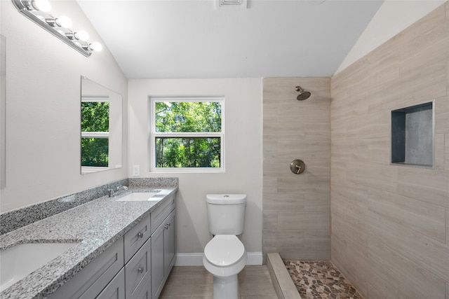 bathroom with tiled shower, toilet, vaulted ceiling, and double vanity