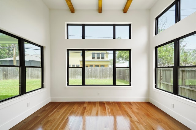 unfurnished room featuring light wood-type flooring, a towering ceiling, and beamed ceiling