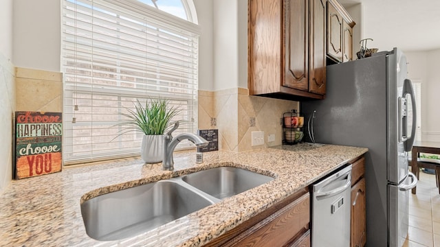 kitchen with sink, light tile patterned floors, appliances with stainless steel finishes, backsplash, and light stone countertops