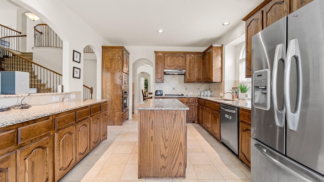 kitchen with sink, backsplash, stainless steel appliances, light stone counters, and a kitchen island