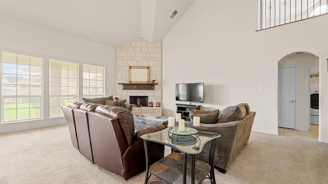 living room with light carpet, washer / clothes dryer, a stone fireplace, and high vaulted ceiling