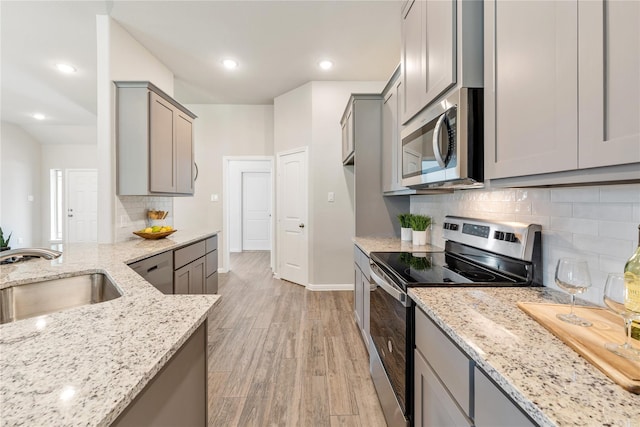 kitchen with gray cabinets, decorative backsplash, light stone countertops, appliances with stainless steel finishes, and light hardwood / wood-style flooring