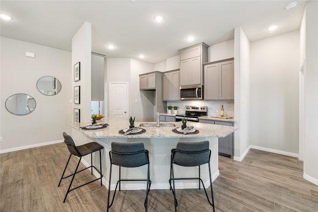 kitchen featuring a kitchen bar, gray cabinetry, appliances with stainless steel finishes, and light hardwood / wood-style floors