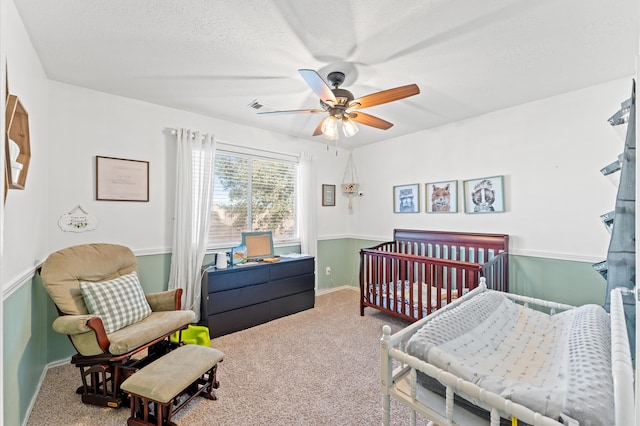 carpeted bedroom with ceiling fan and a nursery area