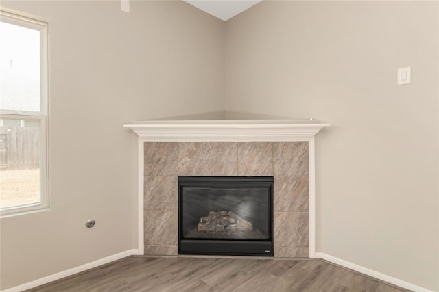 room details with baseboards, a tiled fireplace, and wood finished floors