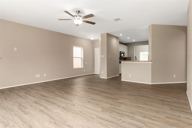 unfurnished living room featuring visible vents, ceiling fan, baseboards, and wood finished floors