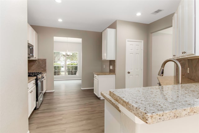 kitchen with a chandelier, stainless steel appliances, a peninsula, white cabinets, and tasteful backsplash