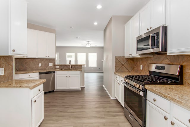 kitchen featuring light stone counters, a sink, white cabinets, appliances with stainless steel finishes, and light wood finished floors