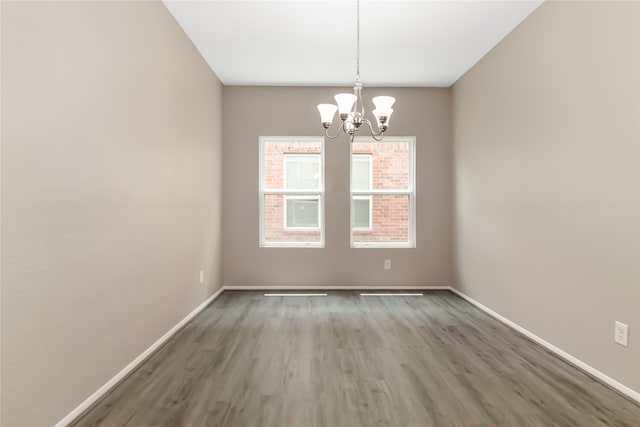 empty room featuring a chandelier, baseboards, and wood finished floors