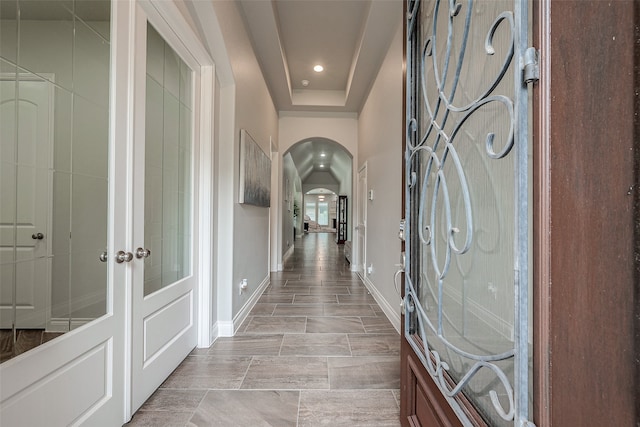 corridor with light tile patterned floors and a tray ceiling