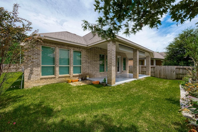 back of house with brick siding, a patio area, a lawn, and fence