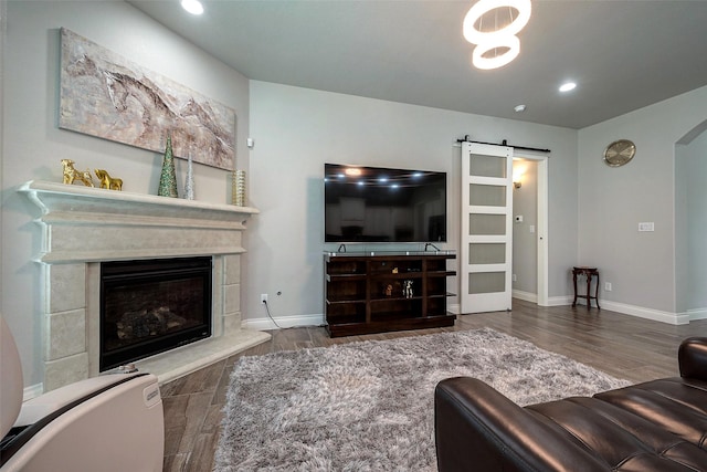 living room with wood finished floors, baseboards, arched walkways, a glass covered fireplace, and a barn door