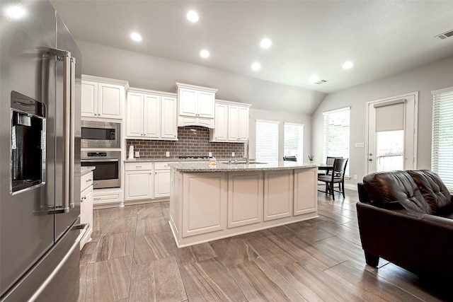 kitchen featuring backsplash, open floor plan, appliances with stainless steel finishes, white cabinetry, and a sink