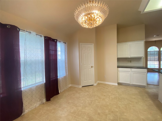 interior space with a notable chandelier, white cabinets, vaulted ceiling, and light tile patterned floors