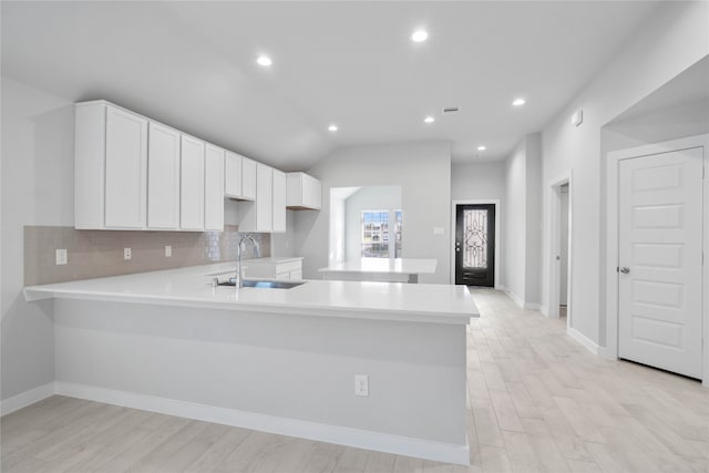 kitchen with kitchen peninsula, sink, white cabinets, light hardwood / wood-style floors, and lofted ceiling