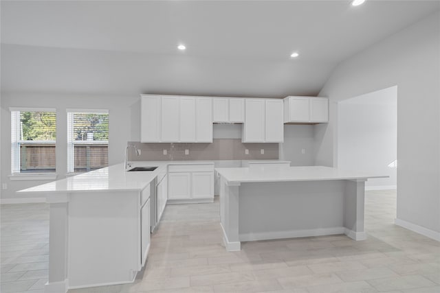 kitchen featuring kitchen peninsula, sink, white cabinets, a center island, and lofted ceiling