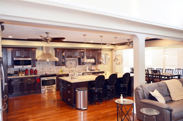 kitchen with range, a breakfast bar area, wall chimney range hood, dark hardwood / wood-style floors, and ceiling fan