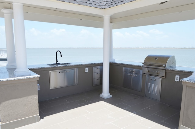 view of patio with grilling area, a water view, sink, and an outdoor kitchen