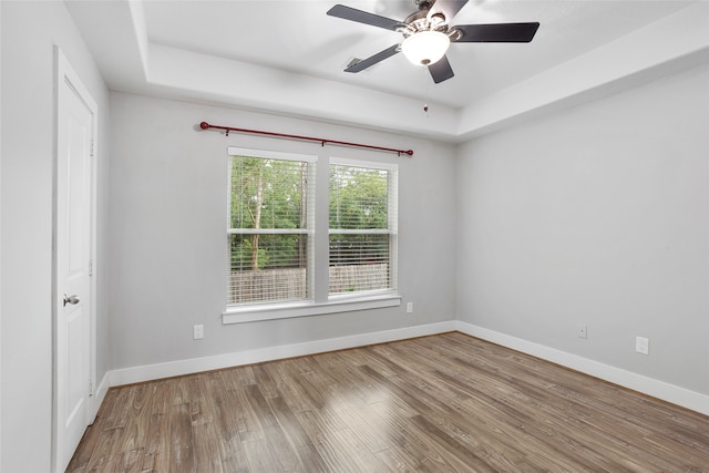 spare room with wood-type flooring, a tray ceiling, and ceiling fan