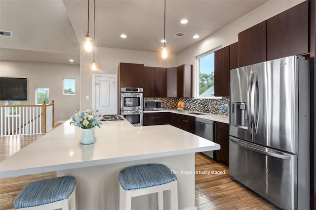 kitchen featuring light wood-type flooring, tasteful backsplash, appliances with stainless steel finishes, and a kitchen bar