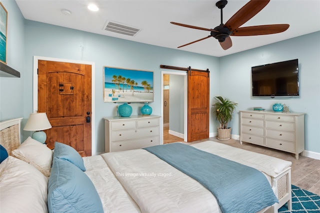 bedroom featuring ceiling fan, light hardwood / wood-style flooring, and a barn door