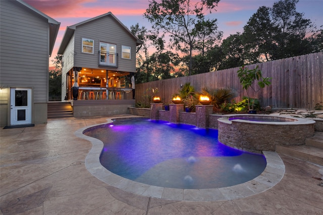 pool at dusk featuring a patio area, pool water feature, and an in ground hot tub