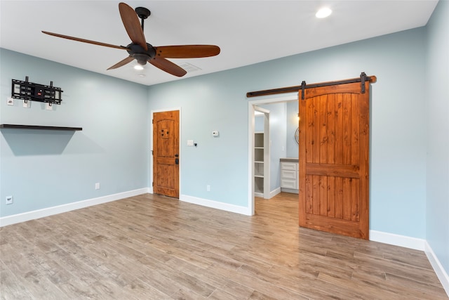 unfurnished room featuring light hardwood / wood-style floors, a barn door, and ceiling fan