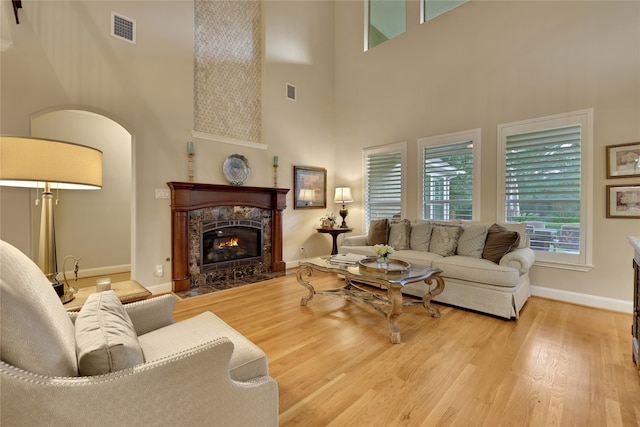 living room featuring light wood-type flooring, a fireplace, and a high ceiling