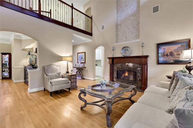 living room featuring crown molding, light wood-type flooring, a towering ceiling, and a high end fireplace