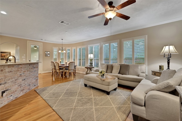 living room featuring light wood-type flooring, ceiling fan, sink, and crown molding