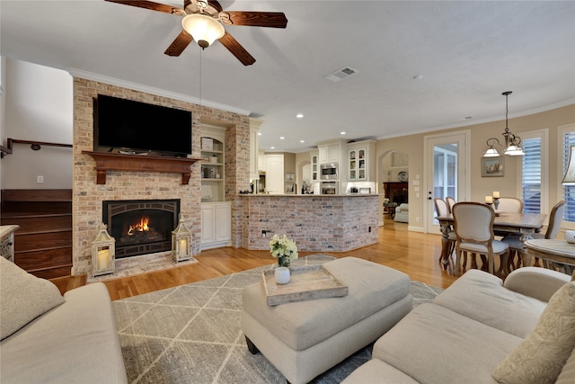 living room featuring ornamental molding, light hardwood / wood-style floors, a fireplace, and ceiling fan