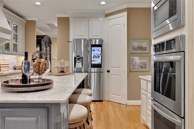 kitchen featuring stainless steel appliances, ornamental molding, a kitchen breakfast bar, and light hardwood / wood-style flooring