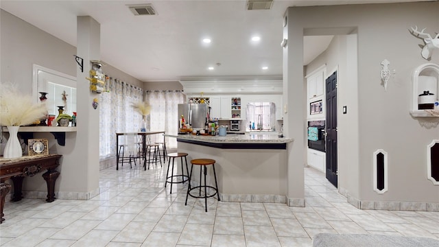 kitchen featuring light tile patterned floors, white cabinets, appliances with stainless steel finishes, a kitchen breakfast bar, and plenty of natural light