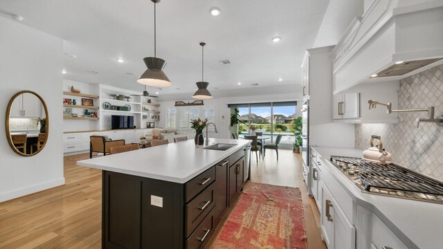 kitchen featuring light hardwood / wood-style flooring, a center island with sink, sink, decorative backsplash, and white cabinetry