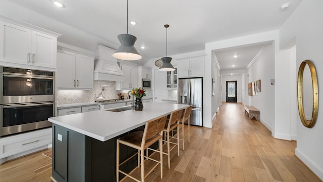 kitchen with light hardwood / wood-style flooring, tasteful backsplash, stainless steel appliances, custom exhaust hood, and a center island with sink