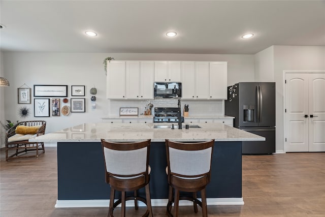 kitchen with tasteful backsplash, hardwood / wood-style floors, sink, fridge with ice dispenser, and an island with sink