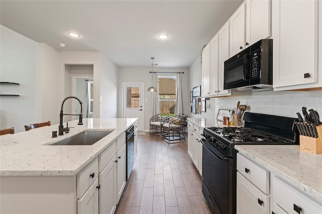 kitchen featuring tasteful backsplash, white cabinets, black appliances, hanging light fixtures, and sink