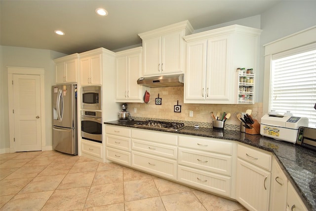 kitchen with backsplash, appliances with stainless steel finishes, light tile patterned floors, and dark stone countertops