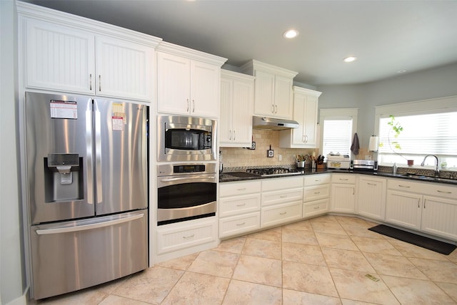 kitchen featuring sink, tasteful backsplash, white cabinetry, dark stone counters, and stainless steel appliances