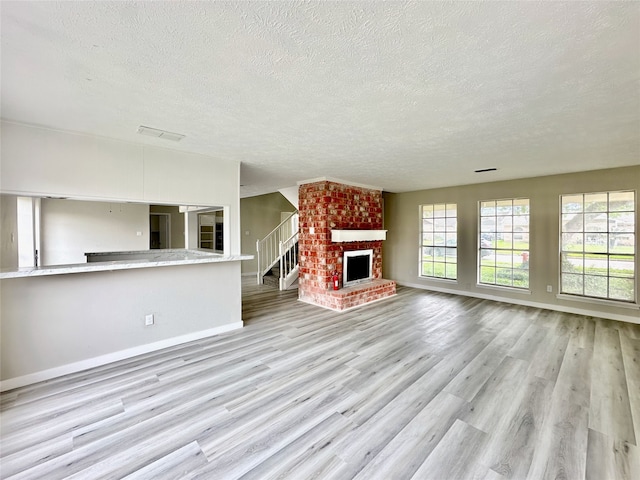 unfurnished living room with light hardwood / wood-style floors, a brick fireplace, brick wall, and a textured ceiling