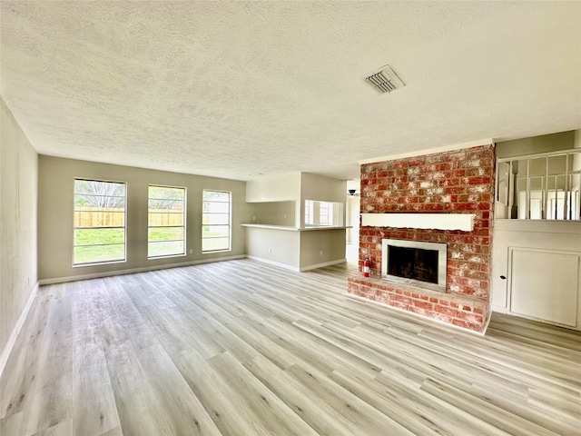 unfurnished living room with brick wall, a fireplace, a textured ceiling, and light hardwood / wood-style floors