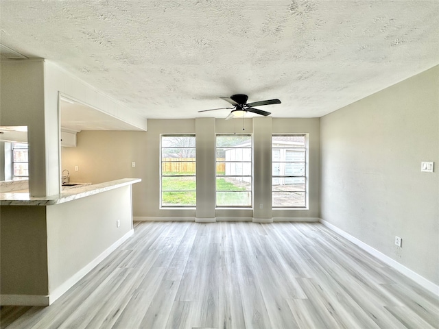 unfurnished room with a textured ceiling, light wood-type flooring, and ceiling fan