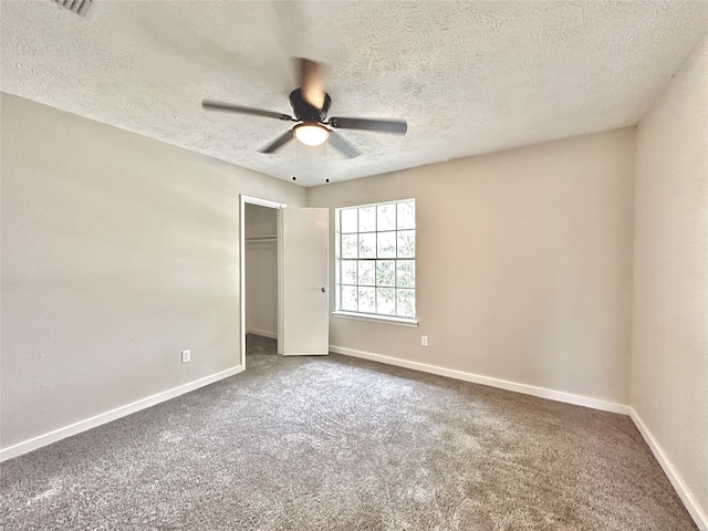 unfurnished bedroom with carpet flooring, a textured ceiling, ceiling fan, and a walk in closet