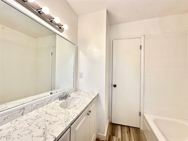 bathroom with a textured ceiling, vanity, tiled shower / bath, and hardwood / wood-style floors